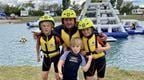 A man with three children in wetsuits and life jackets by a water park